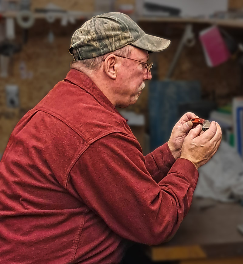 Tom Price sitting at a work table inspecting one of his knives.